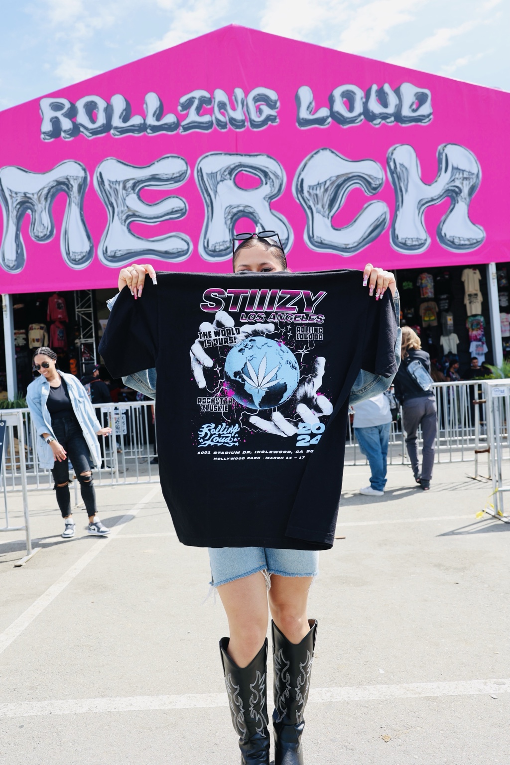 Rolling Loud merch moment with fan holding STIIIZY Los Angeles shirt in front of the Rolling Loud merch tent